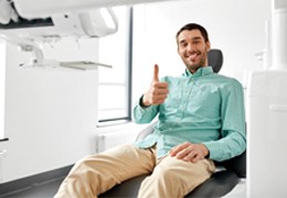 Hombre sonriendo en el sillón dental con el pulgar hacia arriba