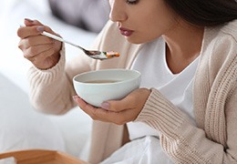 A young woman eating soup after dental implant surgery
