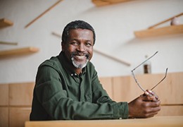 older man holding his glasses and sitting at table 