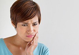 Woman holding cheek in pain before restorative dentistry