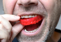 man putting a red mouthguard in his mouth