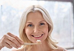 An older woman brushing her teeth after dental implant placement