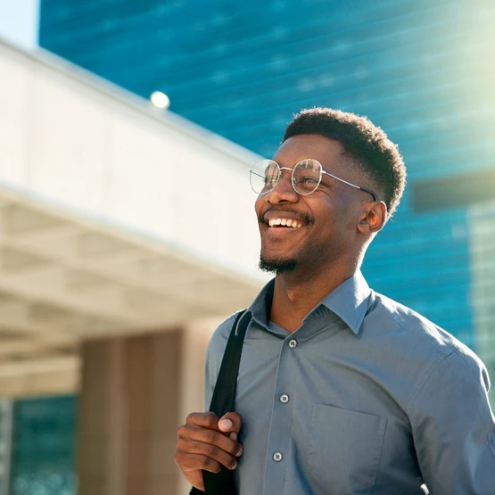 a smiling man wearing glasses with a high rise building in the background