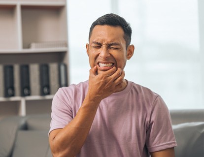 Man squinting in pain holding fingers to the corners of his mouth