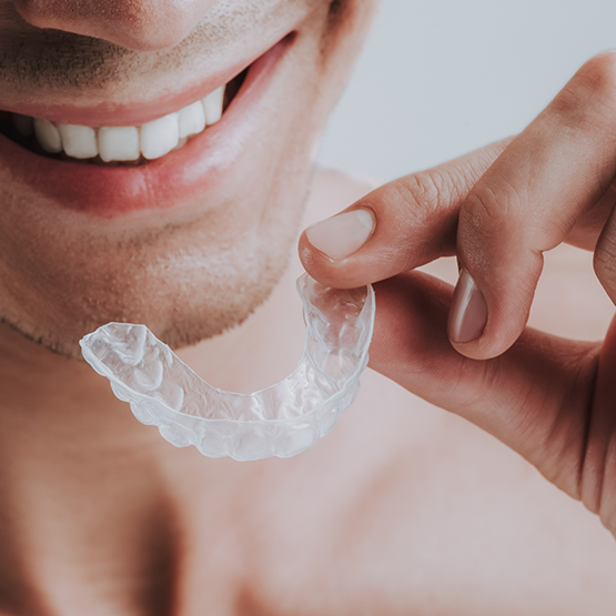 Smiling man holding a nightguard near his teeth