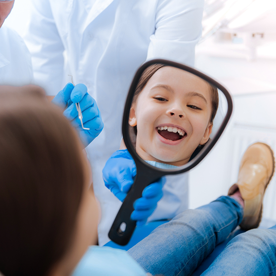Niño mirándose los dientes en un espejo en la silla del dentista