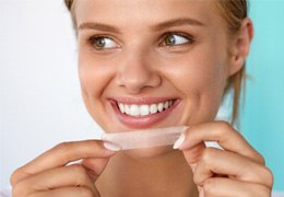 woman smiling while holding whitening strip