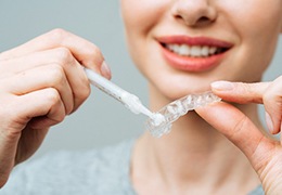 Smiling woman putting whitening gel in custom tray