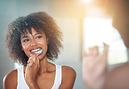 Woman smiling in reflection while brushing her teeth