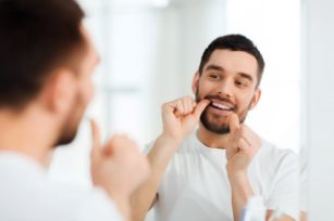 Man flossing in the mirror using tips from a dentist