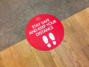 red sticker on ground that says “stay safe and keep your distance” 