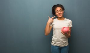 woman with dental insurance in Goodlettsville holding a piggy bank and pointing to her smile