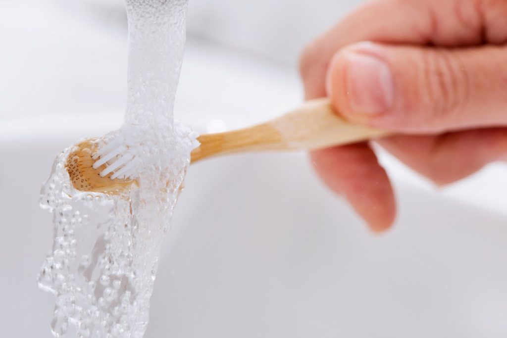 Closeup of patient rinsing their toothbrush with water
