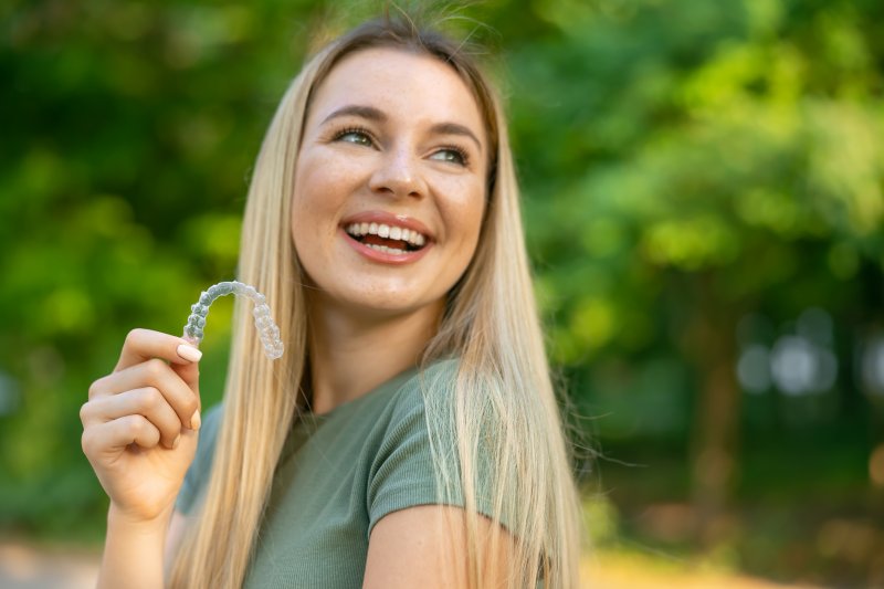 A smiling woman holding a clear aligner outdoors