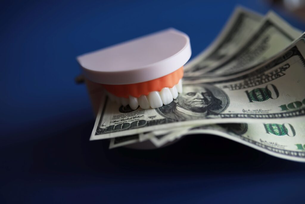 Set of dentures biting $100 bills on dark blue surface