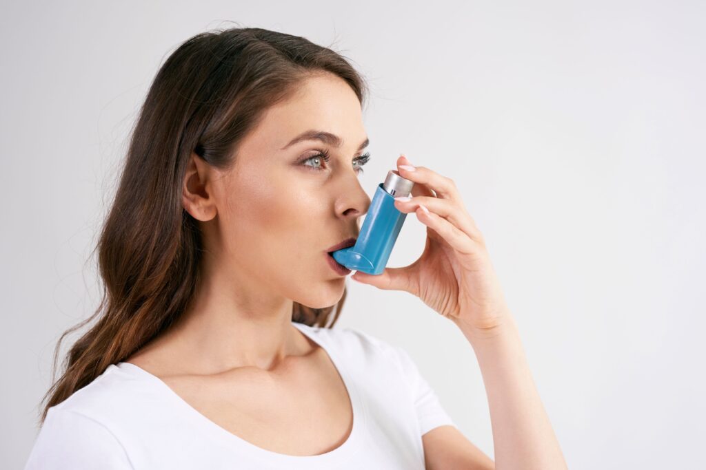 Woman in white shirt using blue asthma inhaler