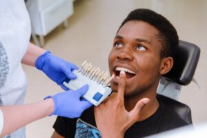 Patient gesturing to teeth while dentist holds different veneers. 
