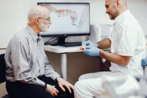 Older patient looking at dentures held by dentist.